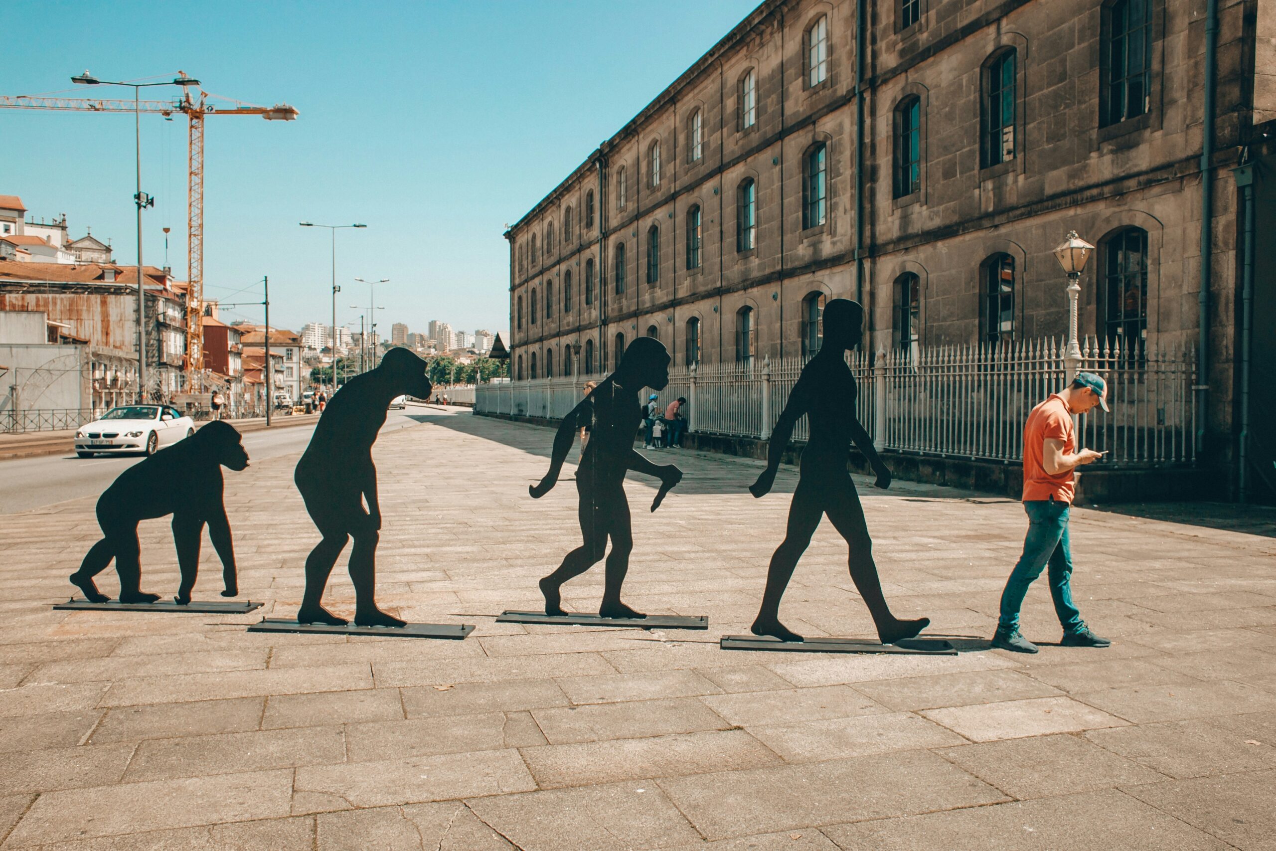 Cut outs of apes in a city with a man in an orange top on his phone to show body image evolution due to social media